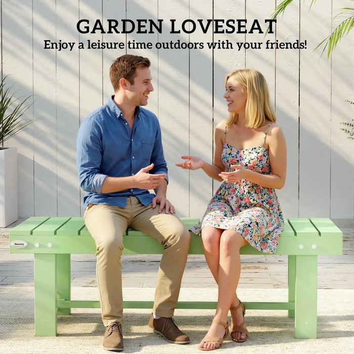 Two people sitting and talking on a light green wooden garden bench outdoors with white wall background