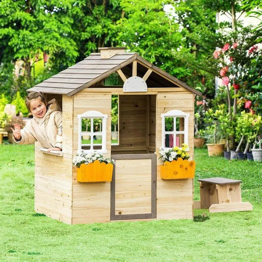 Wooden outdoor playhouse with flower boxes and a child waving from the window in a garden