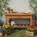 Wooden potting bench with zinc worktop, potted flowers, and gardening tools against a white brick wall