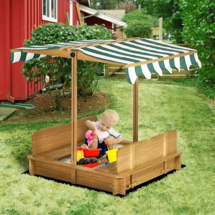 Child playing in wooden sandbox with benches and adjustable canopy in a backyard