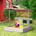 Child playing in a wooden sandbox with kitchen playset and adjustable canopy in a backyard