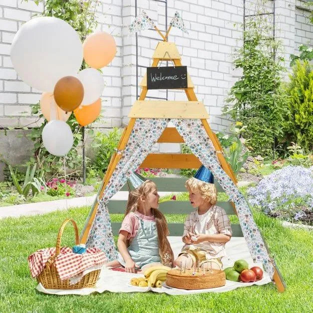 Kids in party hats sitting inside a wooden Montessori teepee tent outdoors with picnic food
