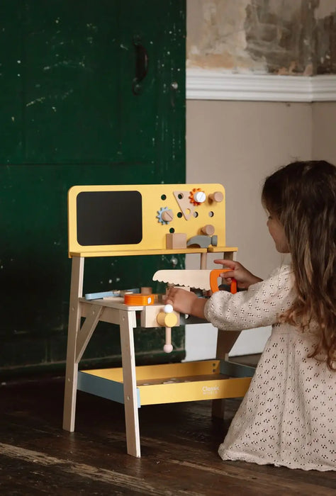 Child playing with Classic World wooden tool bench carpentry playset in a rustic room