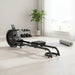 Black rowing machine with a visible brand logo in a plush lounge with weights and plant in the background
