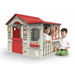 Two children playing in a large outdoor cottage playhouse with red roof and gray walls.