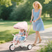 Woman pushing a child in a pink stroller along a path in a park.