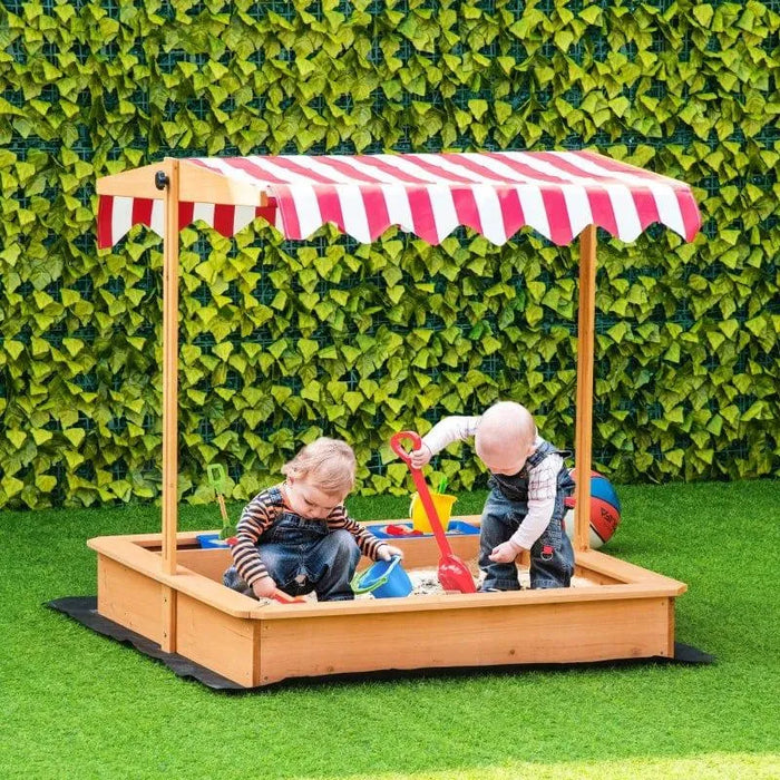 Kids playing in a yellow wooden sandbox with red canopy on green artificial grass