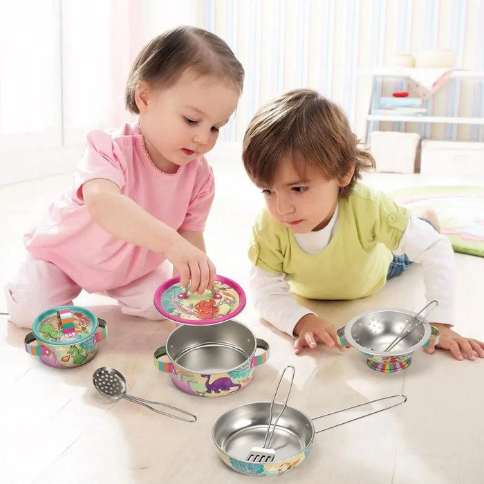 Two toddlers playing with colorful dinosaur tin kitchenware set on the floor indoors