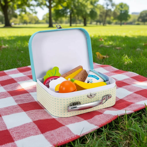 Wooden lunch box playset on picnic blanket outdoors in park, toy food pieces inside.