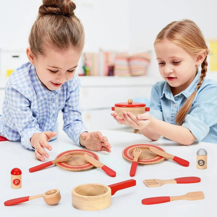 Two children playing with a wooden chef cooking set including utensils, plates, pan, and condiments.