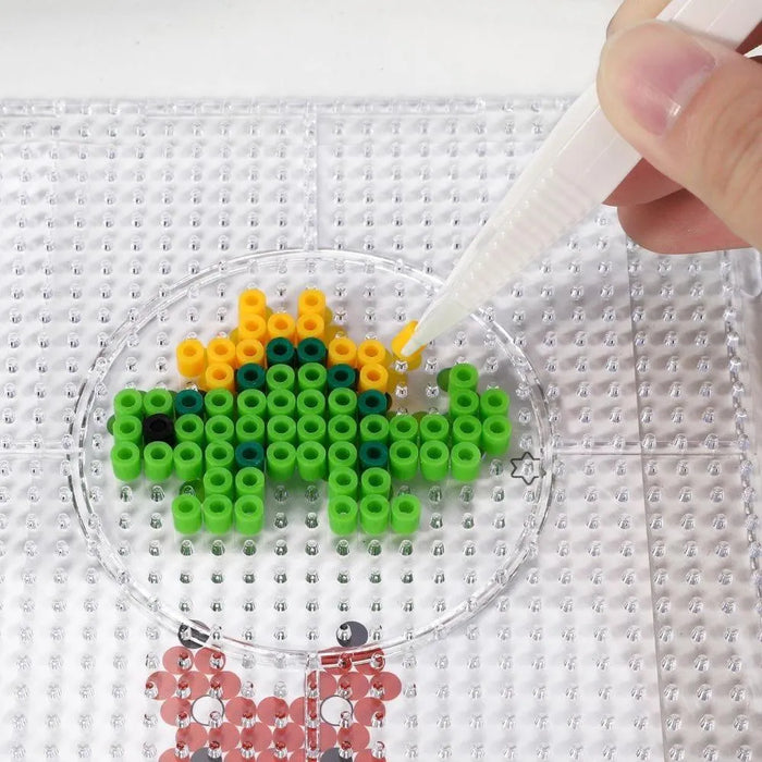 Hand placing yellow bead on dinosaur iron bead art design on clear pegboard