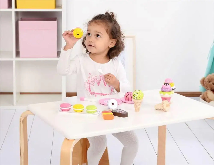 Child playing with wooden ice cream and dessert playset on a white table indoors