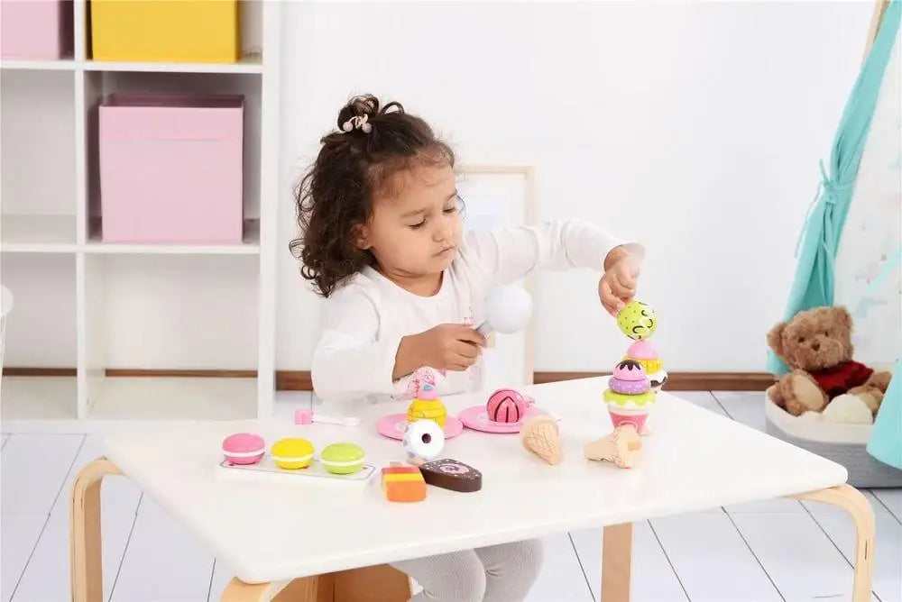Child playing with wooden ice cream and dessert playset on a white table indoors