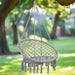 Grey hammock swing chair with tassels and adjustable ropes hanging from a tree outdoors