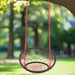 Red and black web swing chair with adjustable ropes hanging from a tree outdoors
