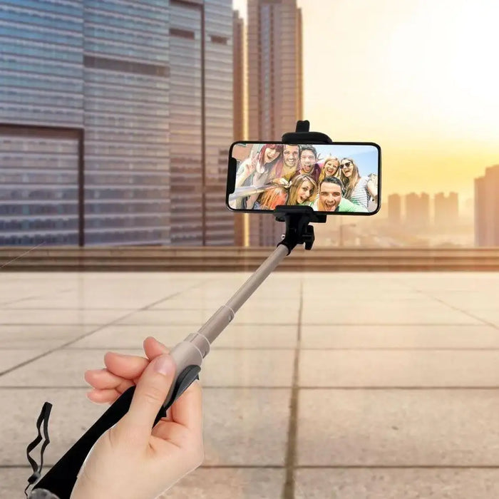 Hand holding an extended Bluetooth selfie stick with phone, city buildings in background
