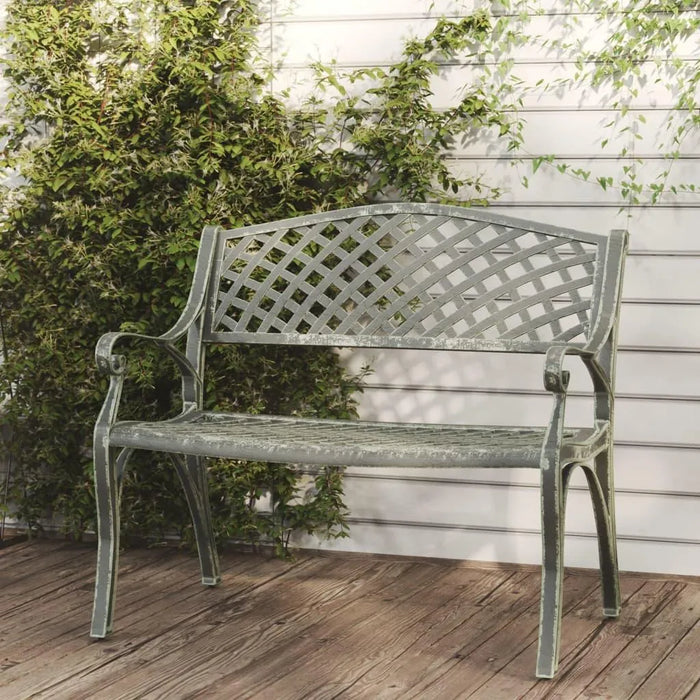 Cast aluminium garden bench with lattice backrest on wooden deck, green foliage in background