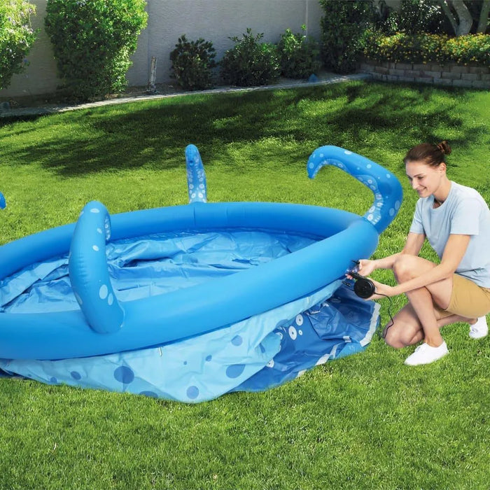 Woman inflating blue octopus-themed inflatable pool with tentacles in backyard lawn.
