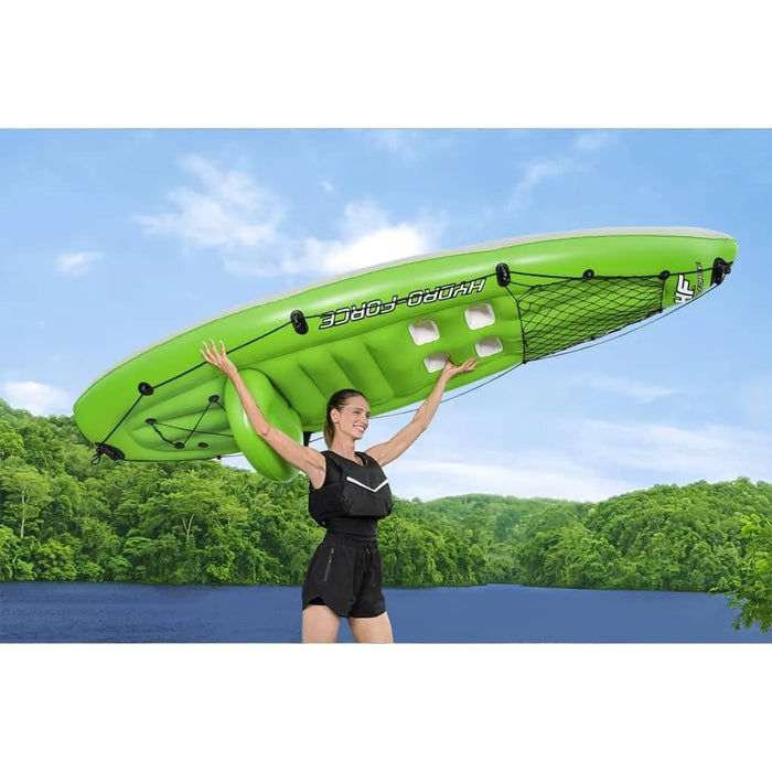 Smiling woman lifting green Hydro-Force inflatable kayak by lake with forest background