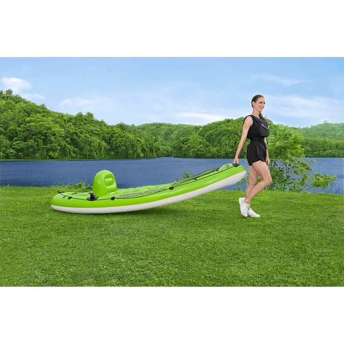 Woman pulling green Hydro-Force inflatable kayak on grass by a lake with forested hills