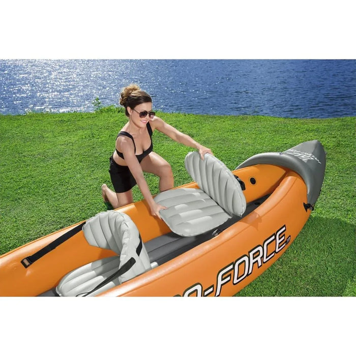 Woman setting up orange Hydro-Force Rapid X2 inflatable kayak by a lake on grass