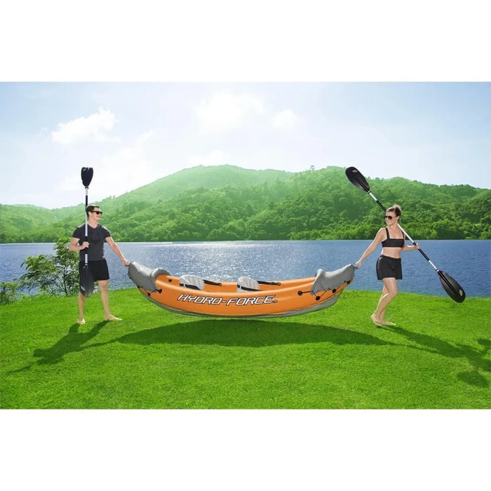 Two people with paddles carrying an orange Hydro-Force inflatable kayak by a lake