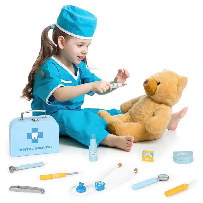 Child in blue dentist costume playing with teddy bear and wooden dental hospital kit