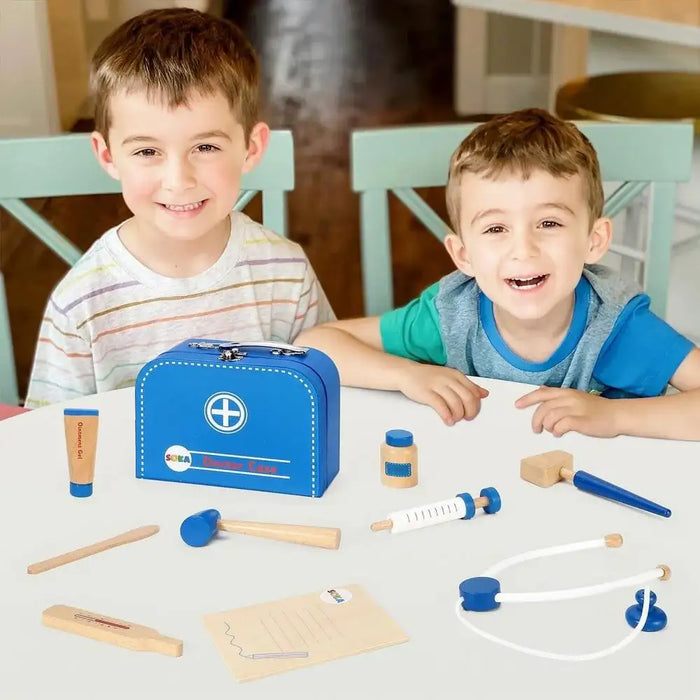 Two smiling children playing with a wooden doctor set and blue carry case on a table.