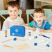 Two smiling children playing with a wooden doctor set and blue carry case on a table.