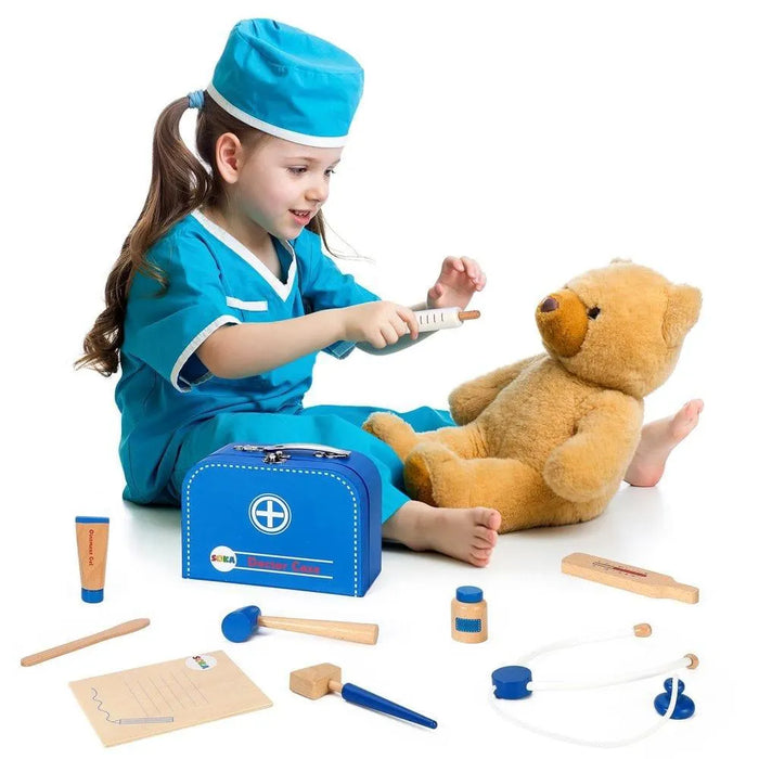 Kid in doctor costume playing with teddy bear and wooden medical role play kit with blue case