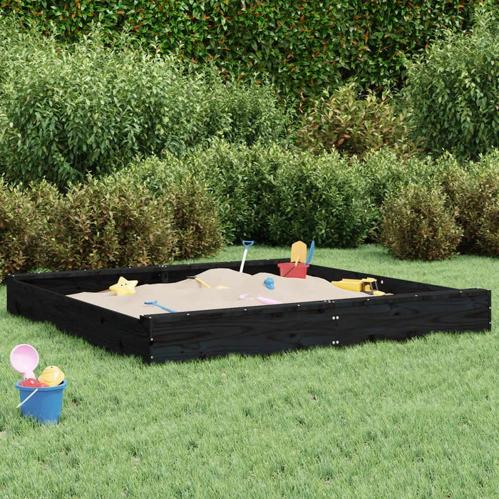Large black wooden sandbox with sand toys on green lawn, bushes in background