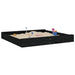 Large square black wooden sandbox with sand toys and built-in seats on white background