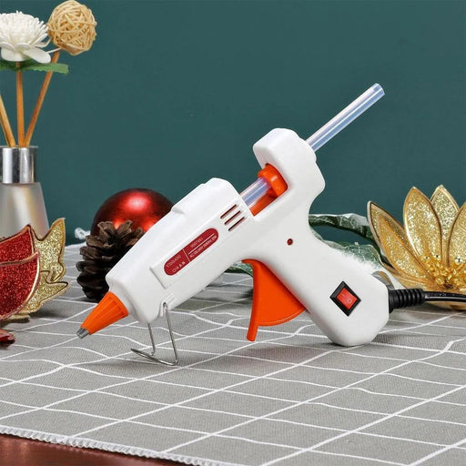 Mini glue gun with glue stick on checkered tablecloth, surrounded by holiday crafts.