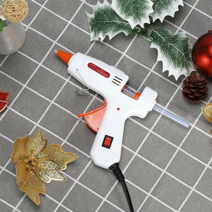 Mini glue gun with glue stick, festive decorations on gray grid tablecloth