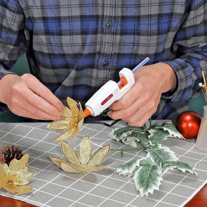 Mini glue gun used for crafting with glitter gold flowers and artificial leaves on table