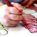 Child coloring with red wax crayon on outlined drawing, close-up hand view
