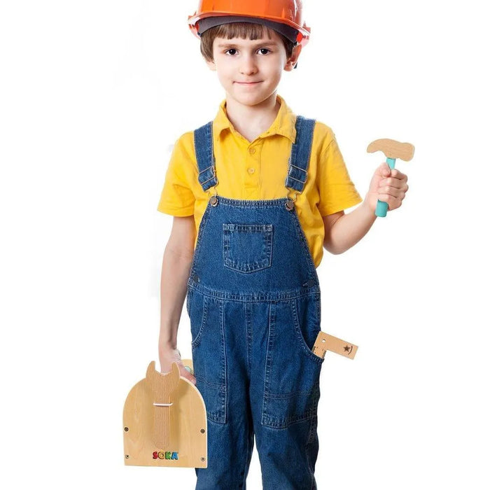 Child in overalls and orange safety helmet holding wooden tool box and toy hammer