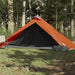 Orange taffeta 1-person camping tent set up on grass in a forest with a chair nearby.