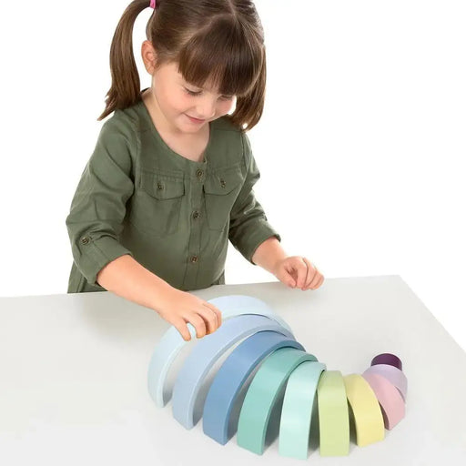 Child playing with pastel wooden rainbow stacker educational toy on white table