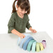 Child playing with pastel wooden rainbow stacker educational toy on white table