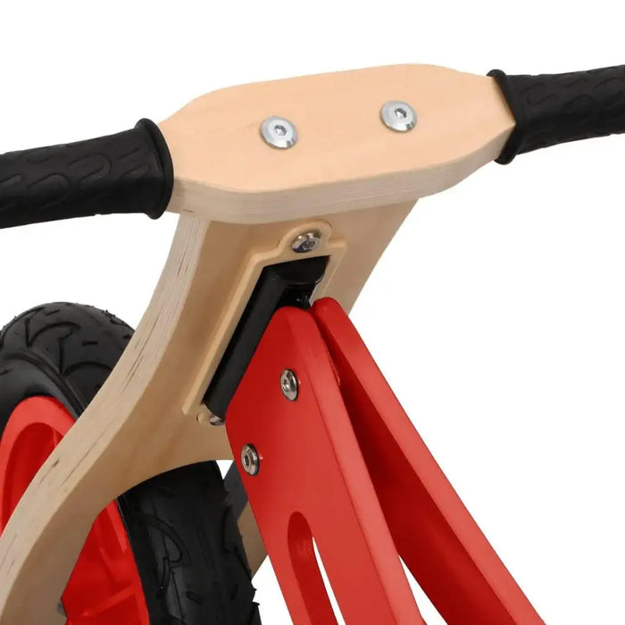 Close-up of wooden and red metal balance bike handlebars with black grips and wheel.
