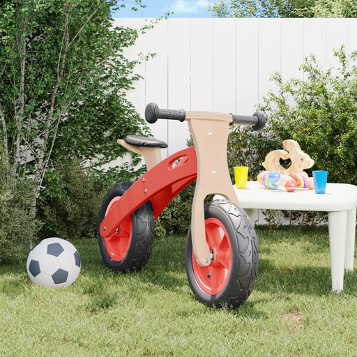 Red balance bike with adjustable seat and handlebar on lawn, soccer ball and toys nearby