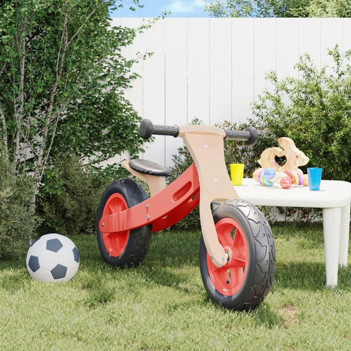 Red balance bike with adjustable seat in a backyard, near a soccer ball and play table.