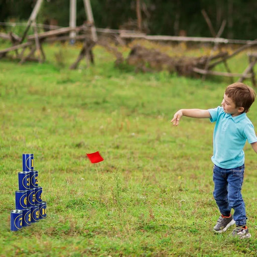 Child playing tin can alley game outdoors, aiming red beanbag at stacked blue cans