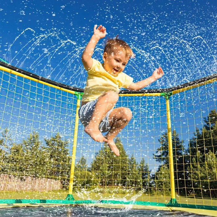 Child jumping on trampoline with water sprinkler outdoors on a sunny day