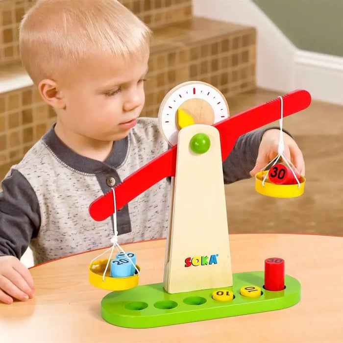 Child playing with wooden Montessori balancing toy weighing scale on table