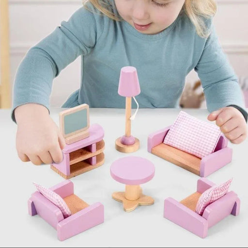 Child playing with pink wooden dollhouse furniture set including sofa, chairs, table, lamp.
