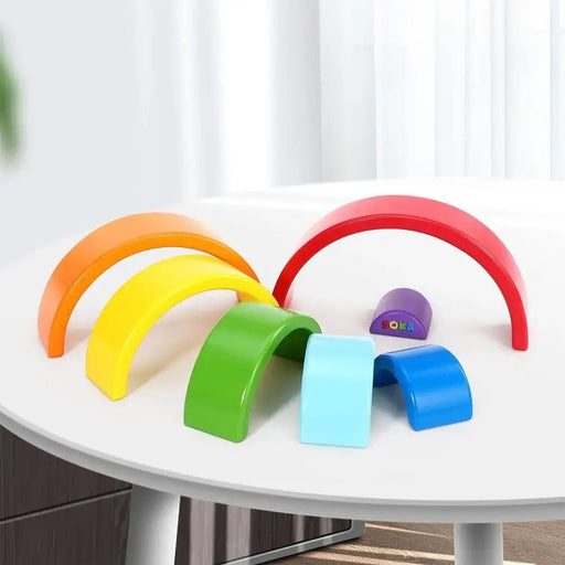 Wooden rainbow stacker toy with seven colorful arches on a white table
