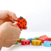 Hands threading a wooden ladybug bead from an educational lacing toy playset with colorful blocks.